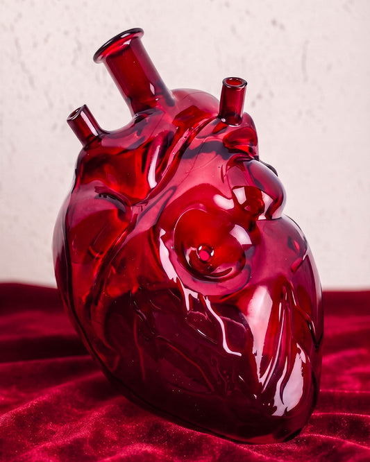 Glossy ruby red anatomical heart-shaped glass pipe with realistic sculpted veins displayed on deep red velvet.