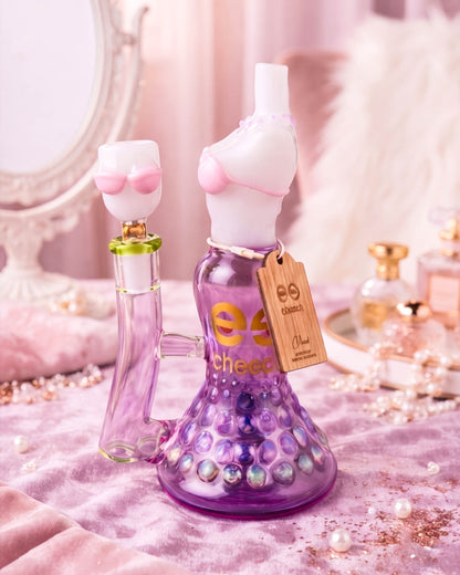 Purple Cheech Glass bikini-shaped beaker bong with sculpted pink details, bubble-textured base, and a 14mm glass bowl on a glamorous vanity display.