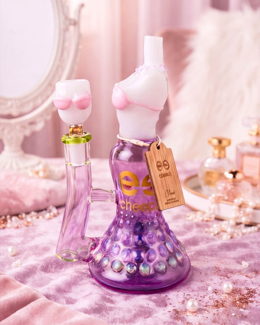 Purple Cheech Glass bikini-shaped beaker bong with sculpted pink details, bubble-textured base, and a 14mm glass bowl on a glamorous vanity display.