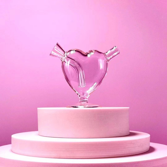 Clear heart-shaped glass blunt bubbler with curved internal downstem and small pedestal base against a pink background.