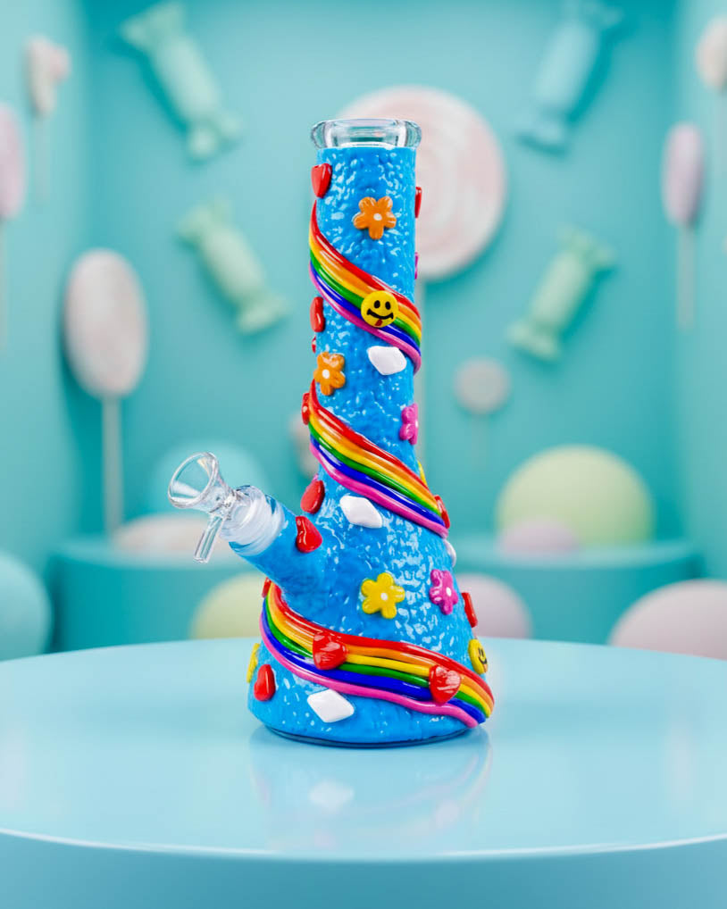 Bright blue 10-inch beaker bong decorated with raised rainbow swirls, colorful flowers, hearts, smiley faces, and a clear 14mm bowl.