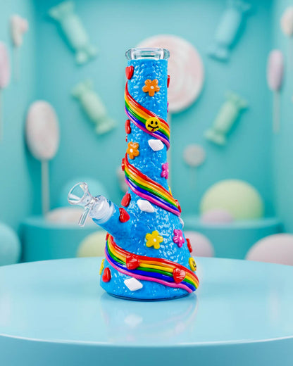 Bright blue 10-inch beaker bong decorated with raised rainbow swirls, colorful flowers, hearts, smiley faces, and a clear 14mm bowl.