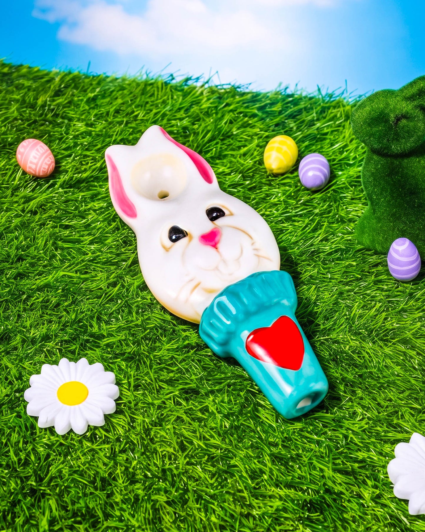 4.5-inch bunny-shaped ceramic hand pipe with white rabbit face, pink ears, turquoise handle, and red heart detail on green grass.